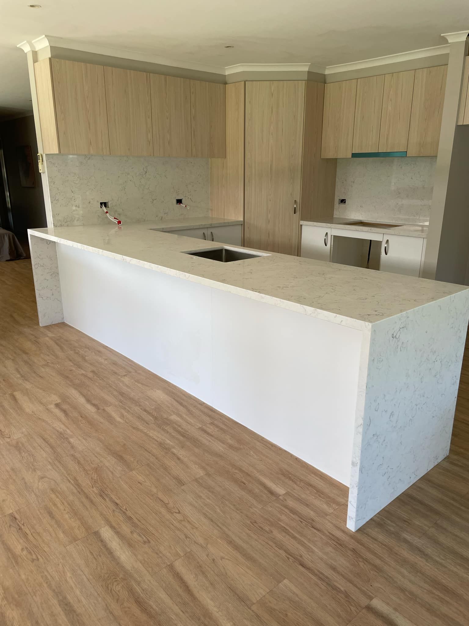 New kitchen with white speckled countertops and island, light wood cabinetry and flooring.