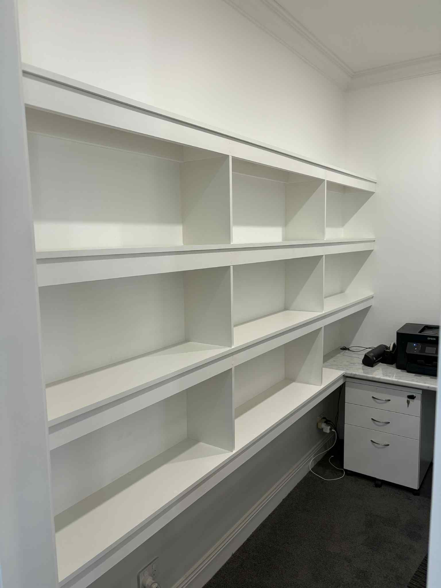 Built-in white bookshelves on a wall. A desk and office equipment are in the corner.
