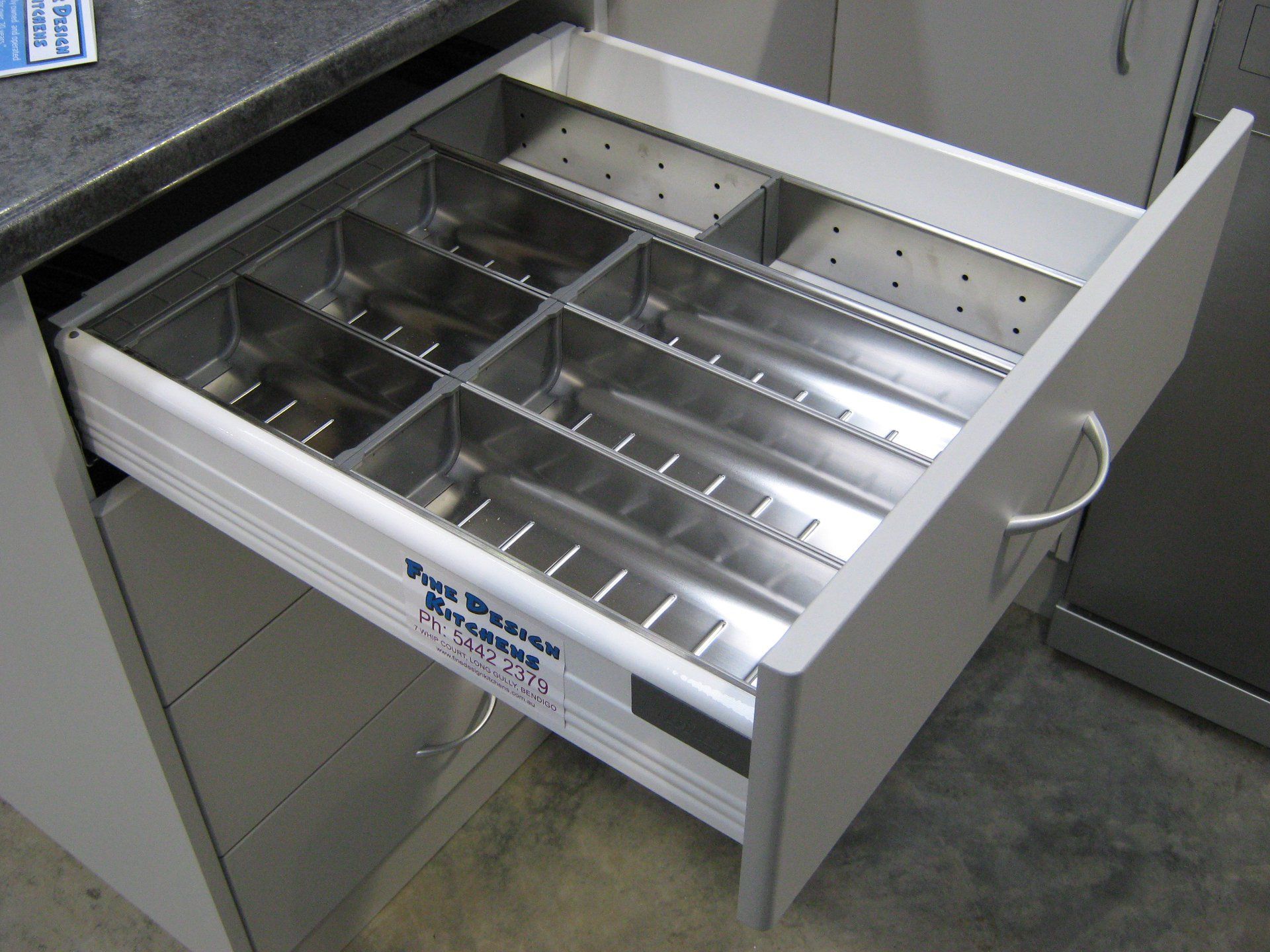 Open kitchen drawer with stainless steel utensil dividers.