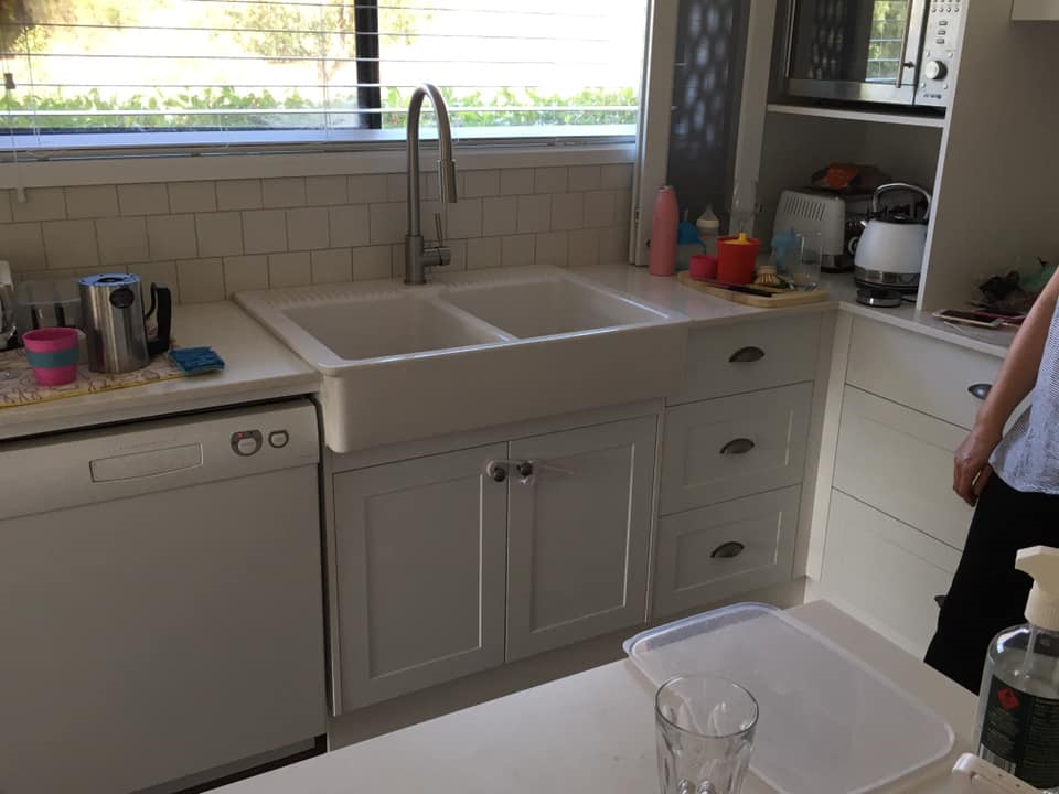 White kitchen with a double sink, dishwasher, and cabinets. A person stands on the right.