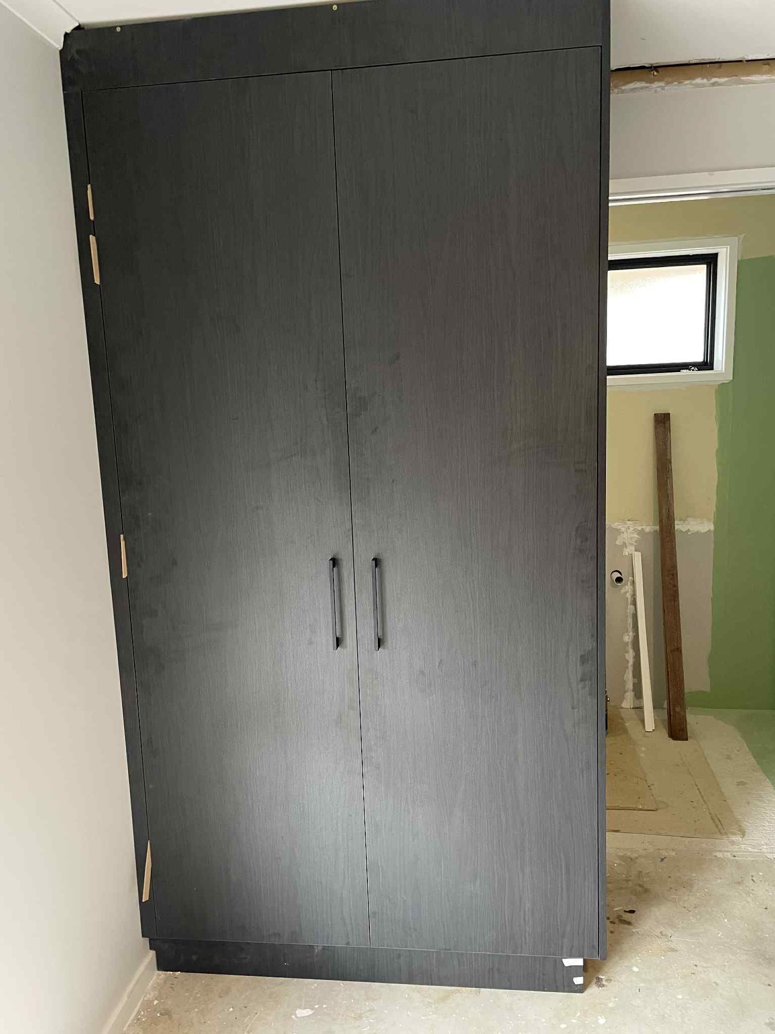 Black cabinet in a room under construction with two doors and handles, unfinished walls and floor.