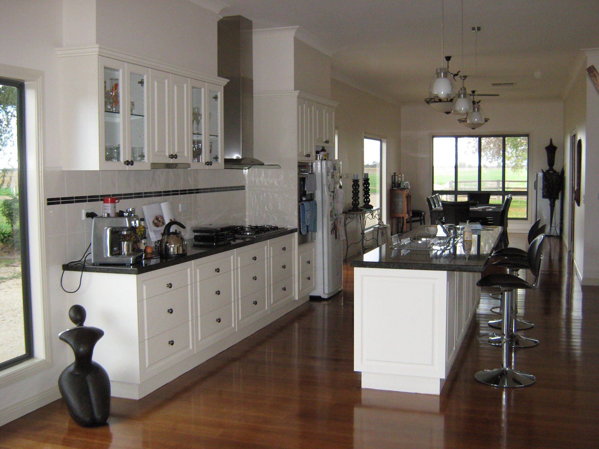 White kitchen with black countertops, stainless steel appliances, and island with bar stools.