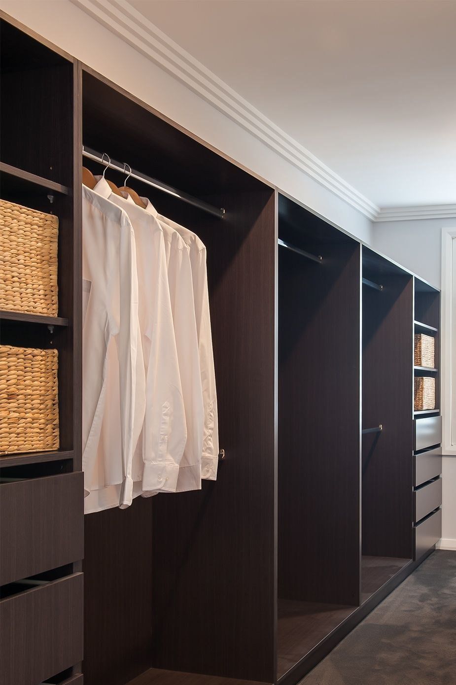 Built-in dark brown closet with hanging white shirts, baskets, and drawers.