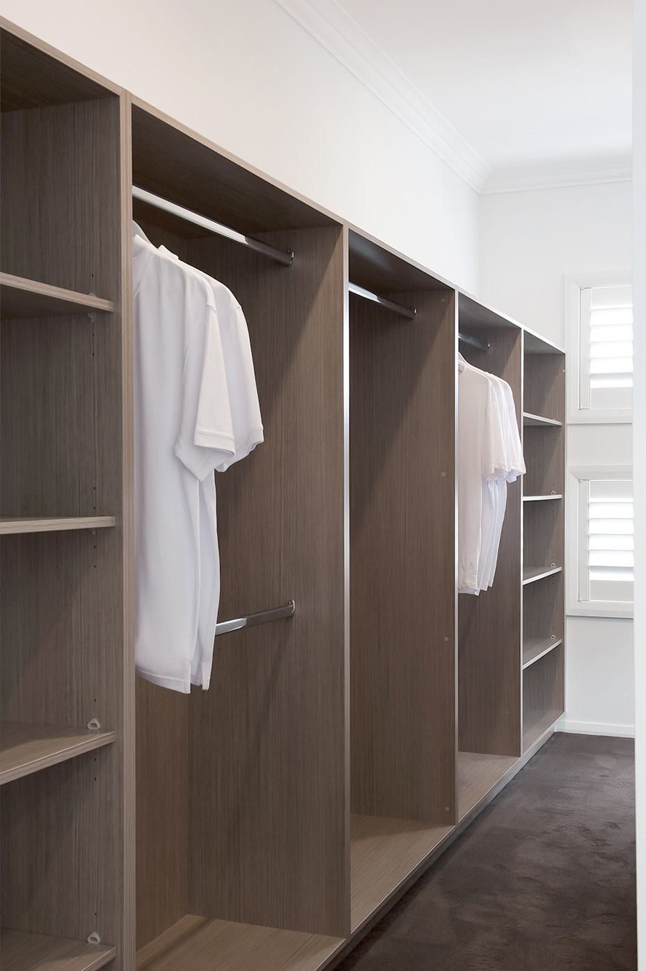 Walk-in closet with built-in shelving and hanging rods. White shirts hang; neutral wood-tone cabinets.