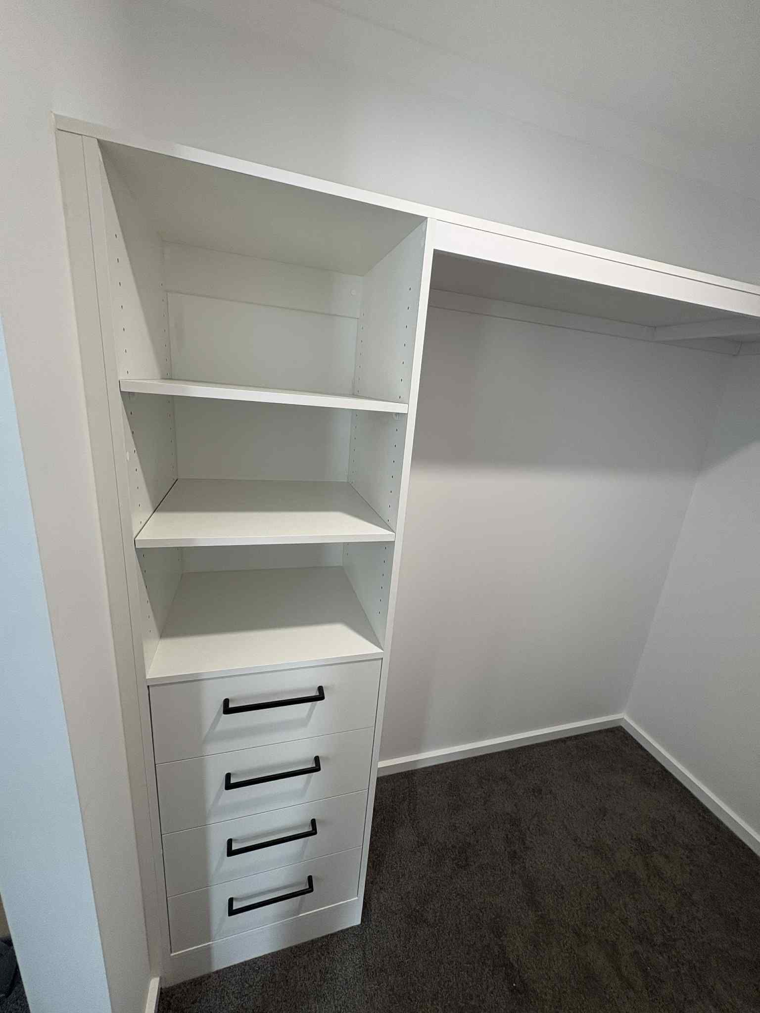White built-in closet with shelves and drawers. Gray carpeted floor. Angled ceiling.