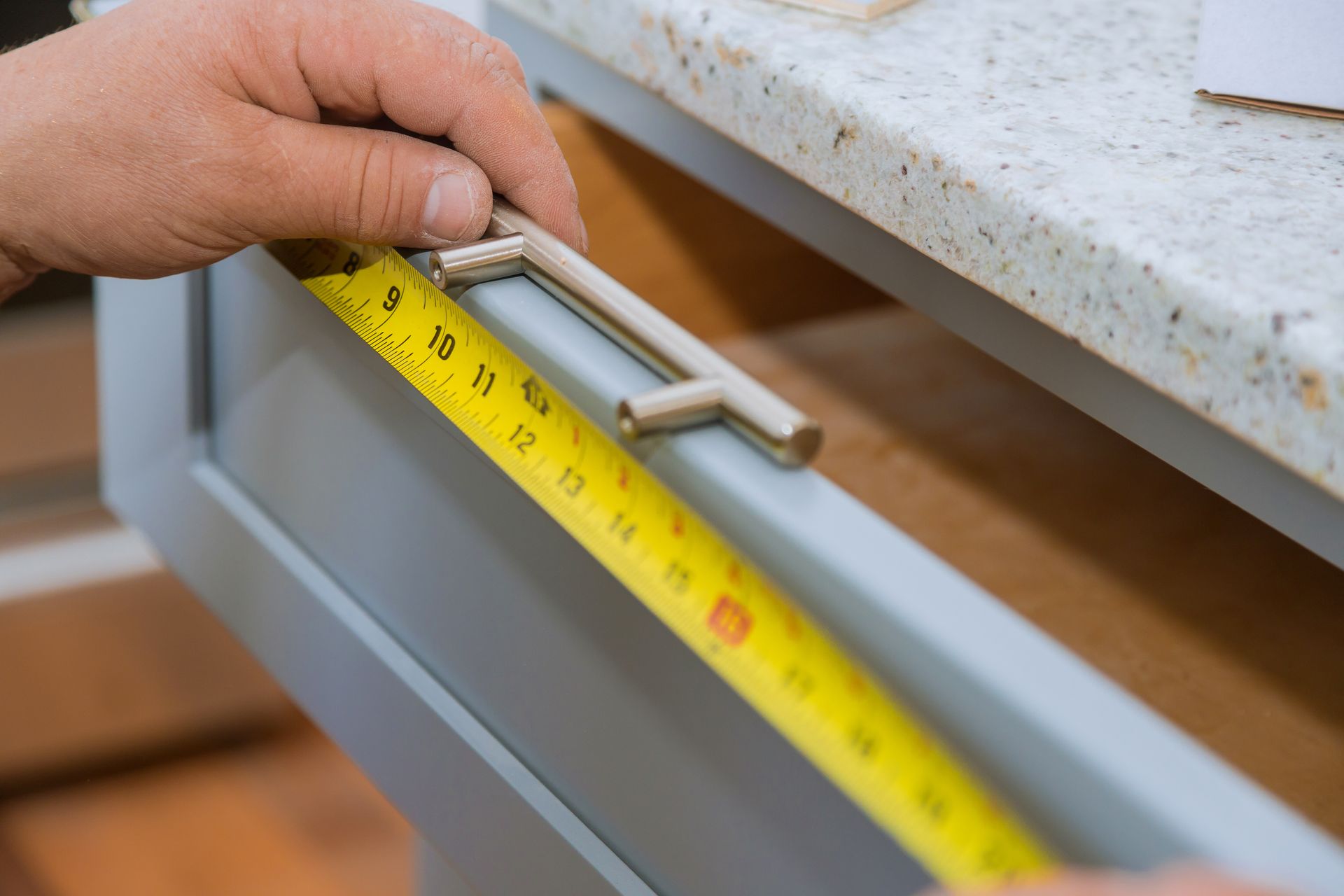 A close-up of a carpenter measuring a drawer with measuring tape.