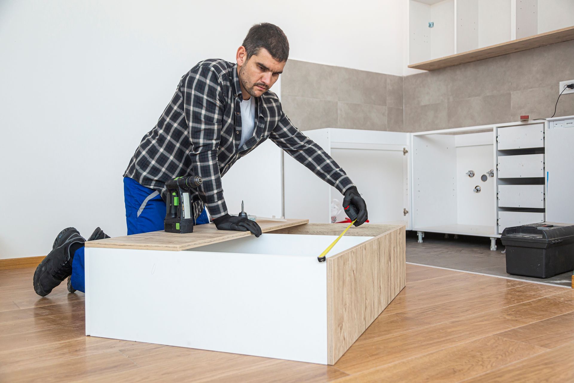 A carpenter measures shelves that are parts of a new kitchen with a meter.