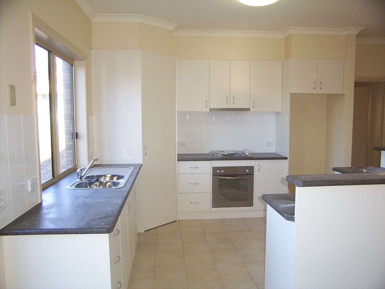 White kitchen with dark countertops, oven, stovetop, and cabinets.