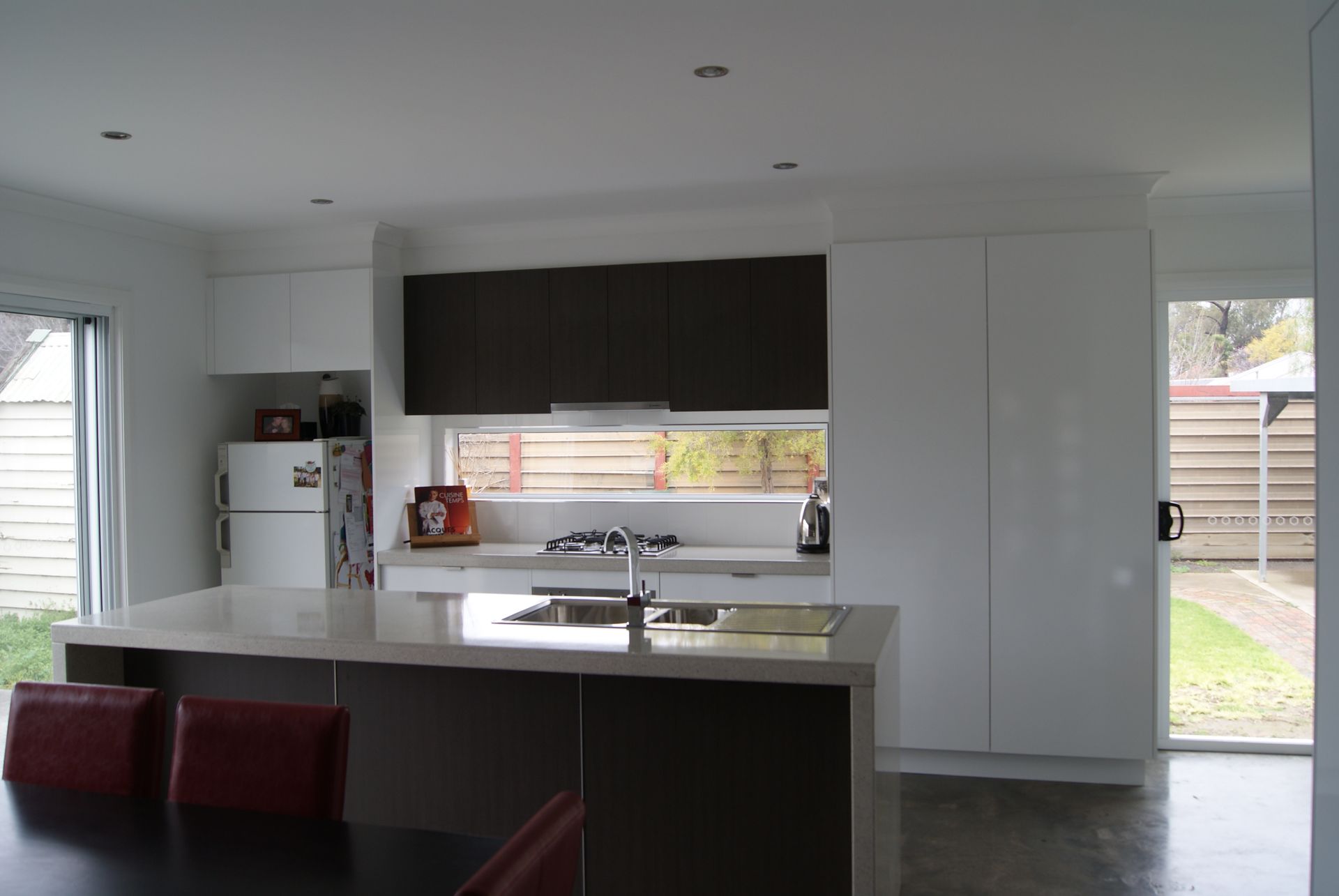 Modern kitchen with white and dark brown cabinets, island with sink, and red chairs.