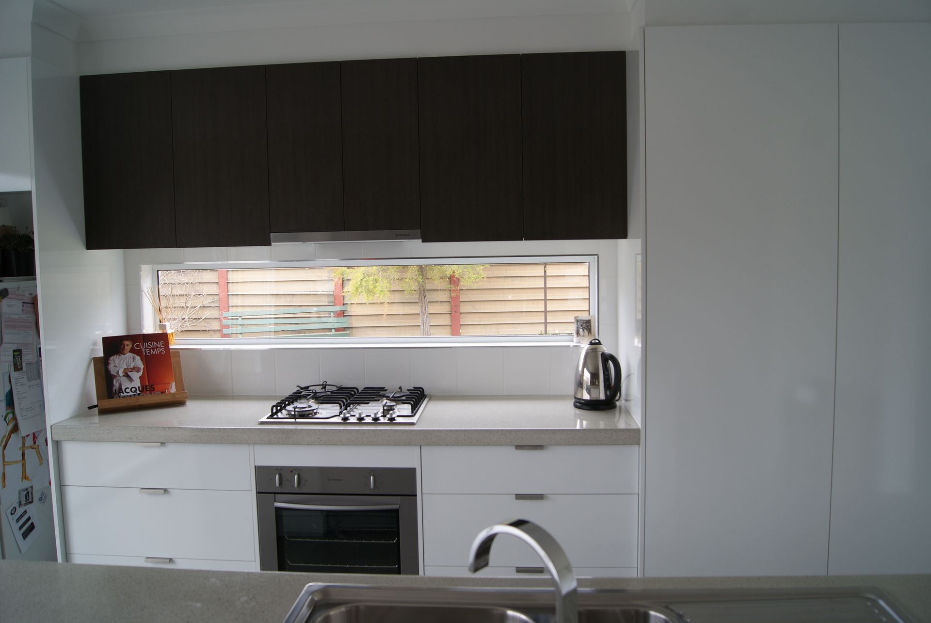 Modern kitchen with white cabinets, dark upper cabinets, stove, oven, window, and sink.