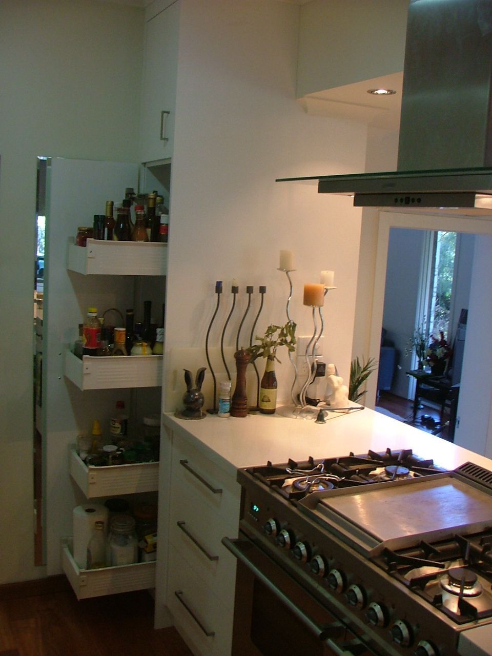 Pull-out pantry with shelves filled with jars/bottles, next to a white countertop and gas stovetop.