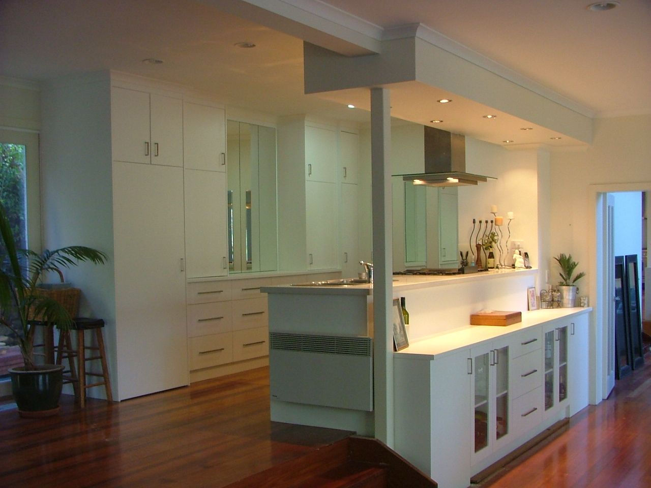 Modern white kitchen with stainless steel appliances, dark wood floors, and cabinets.
