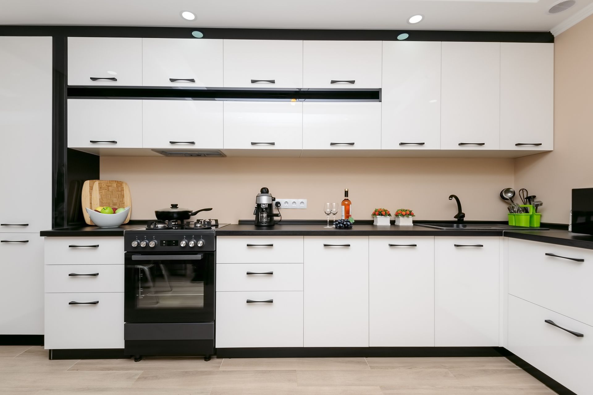 White kitchen cabinets with black countertops and appliances; beige backsplash.