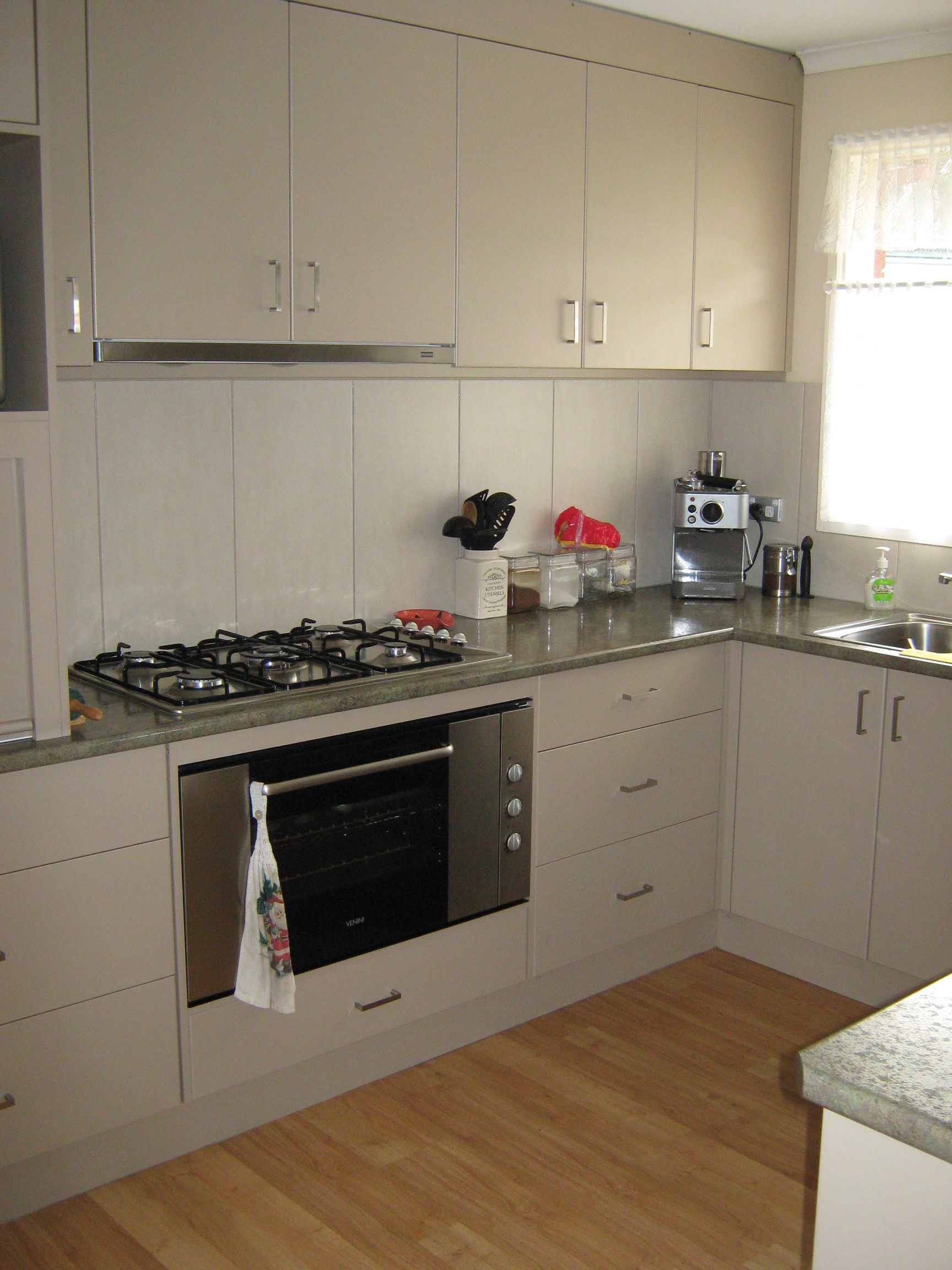 Beige kitchen with stove, oven, cabinets, granite countertop, and wood floor.
