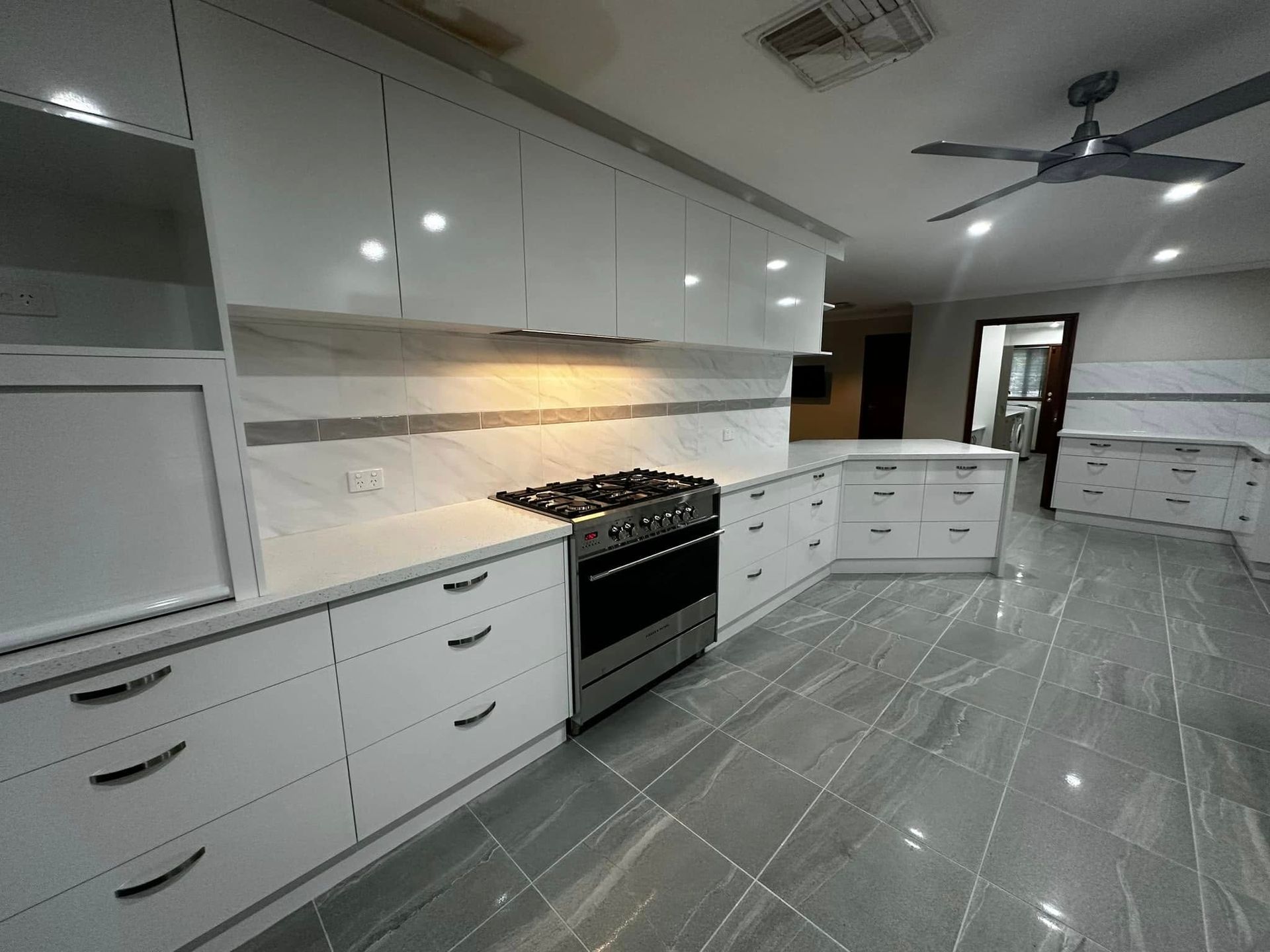 Modern white kitchen with stainless steel appliances, marble backsplash, and gray tile floor.