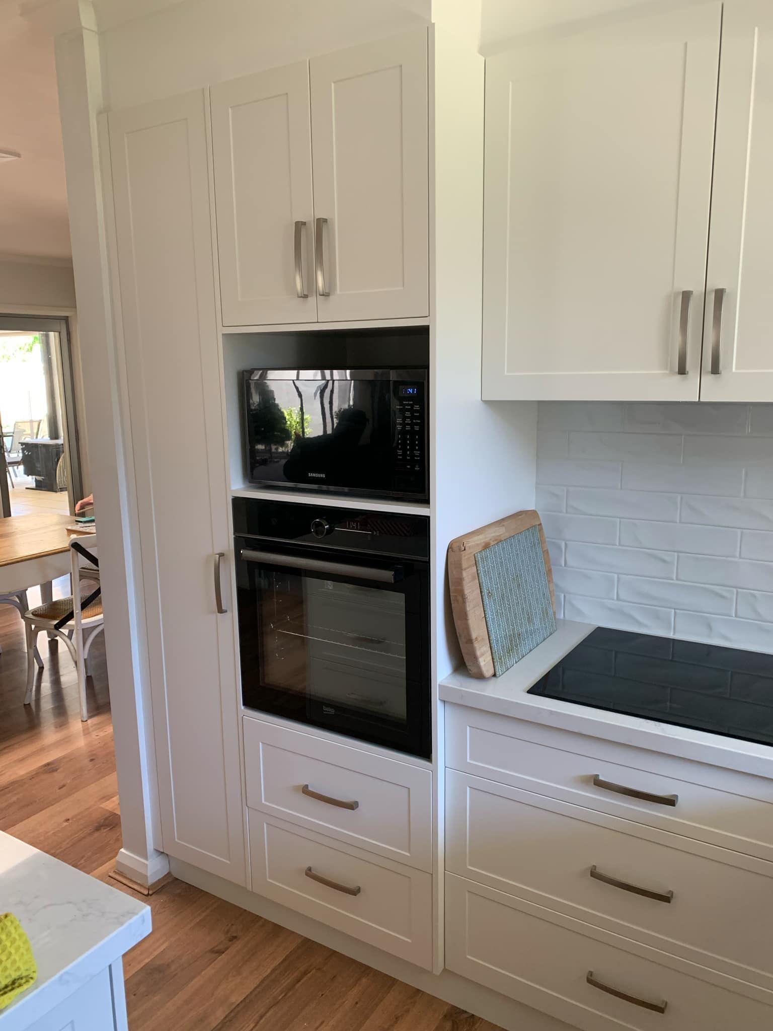 White kitchen cabinetry with built-in oven and microwave. Countertop with stovetop and backsplash.