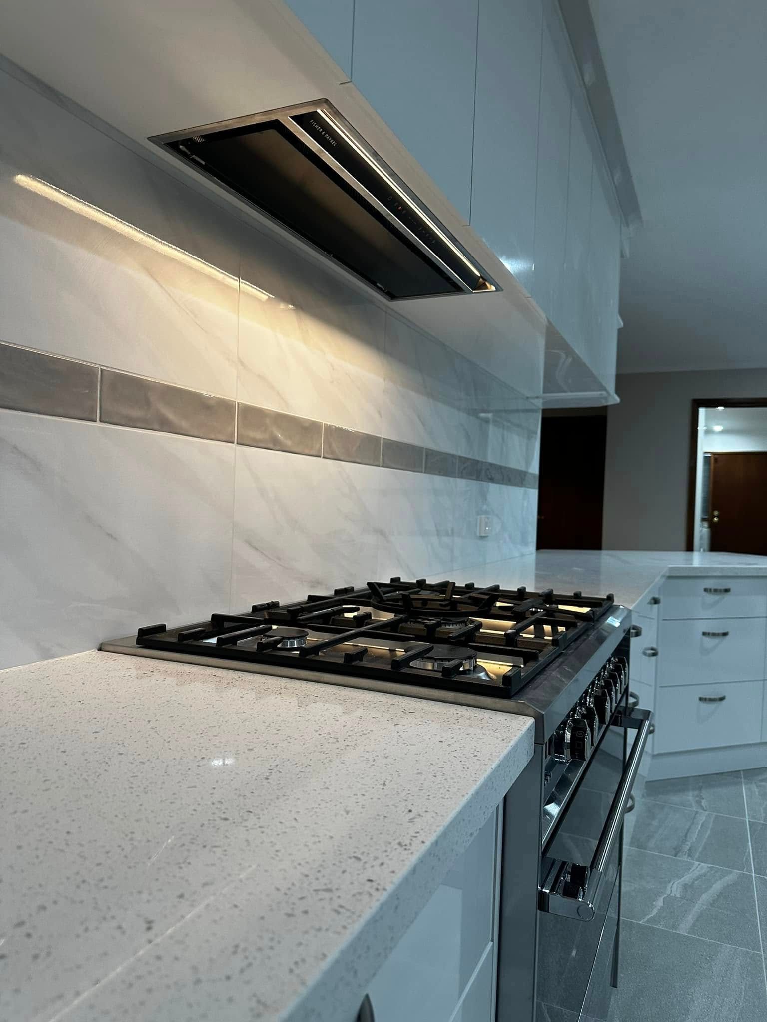 Kitchen with cooktop, range hood, and white countertops. Backsplash of white and gray tiles.