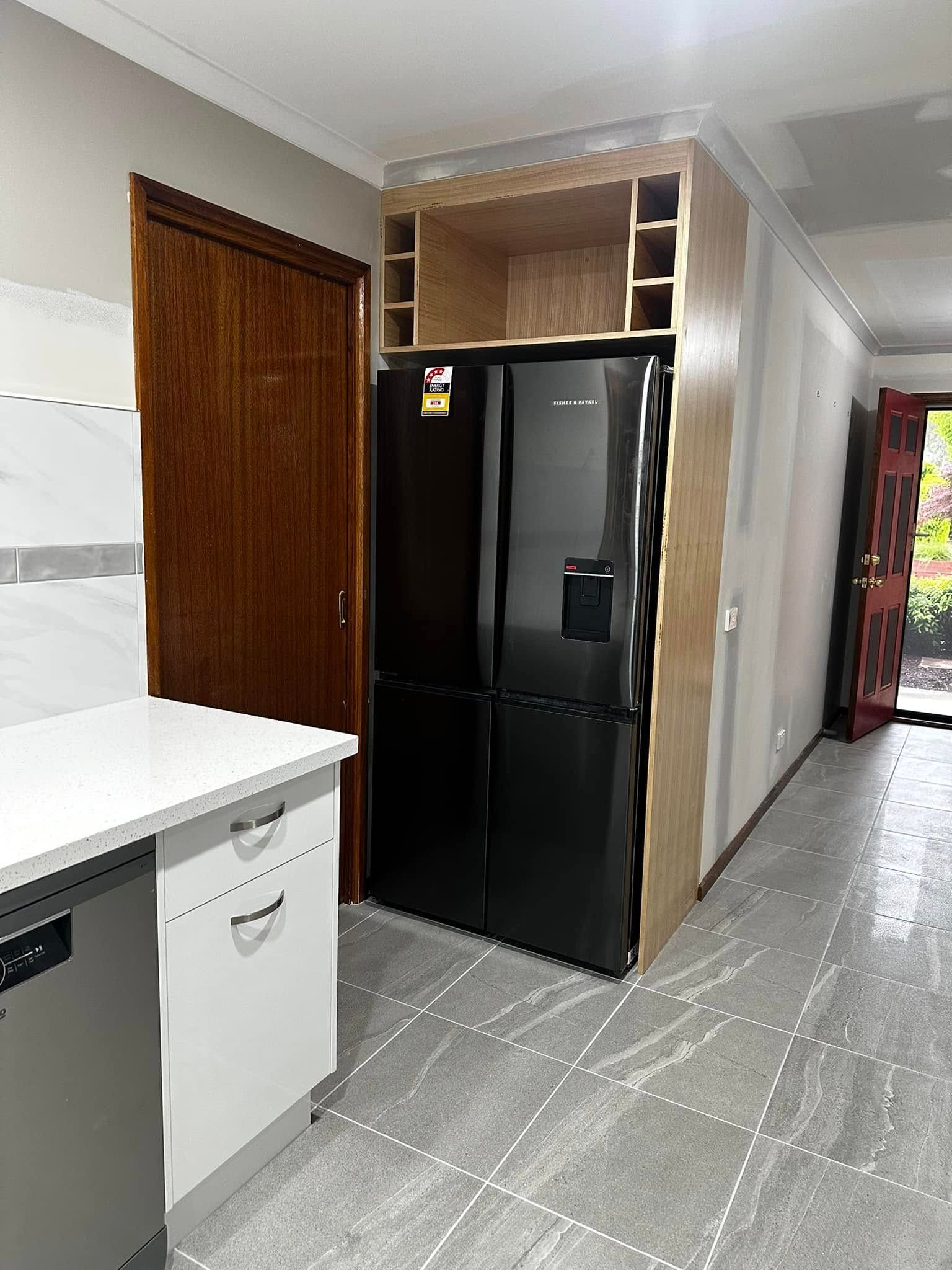 Kitchen with a black refrigerator built into light wood cabinetry; door and countertop visible.