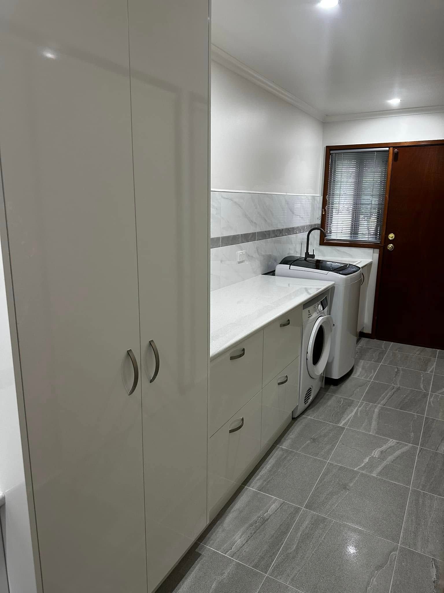 White laundry room with cabinets, washing machine, sink, and closed wooden door.