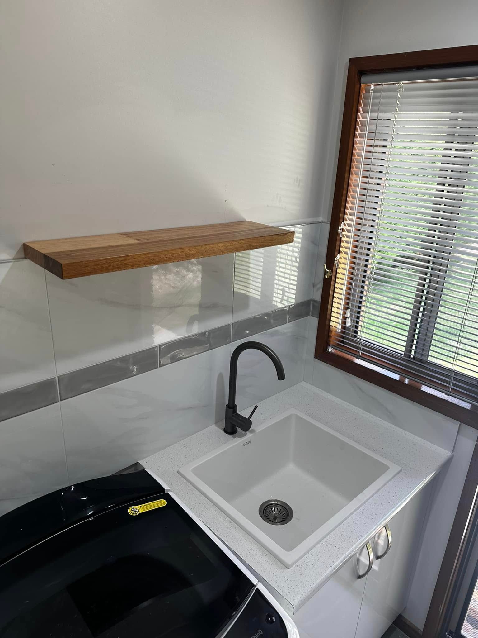 Laundry room with white sink, black faucet, wooden shelf, and window with blinds.