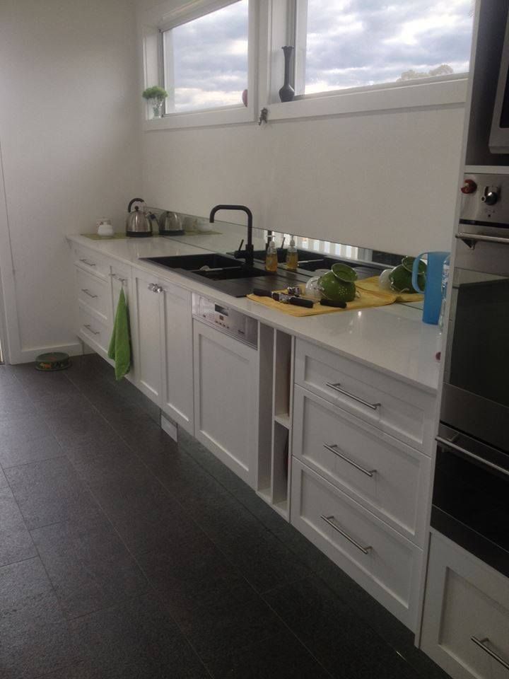 White kitchen cabinets with black sink and faucet, dishwasher, and countertops under a window.