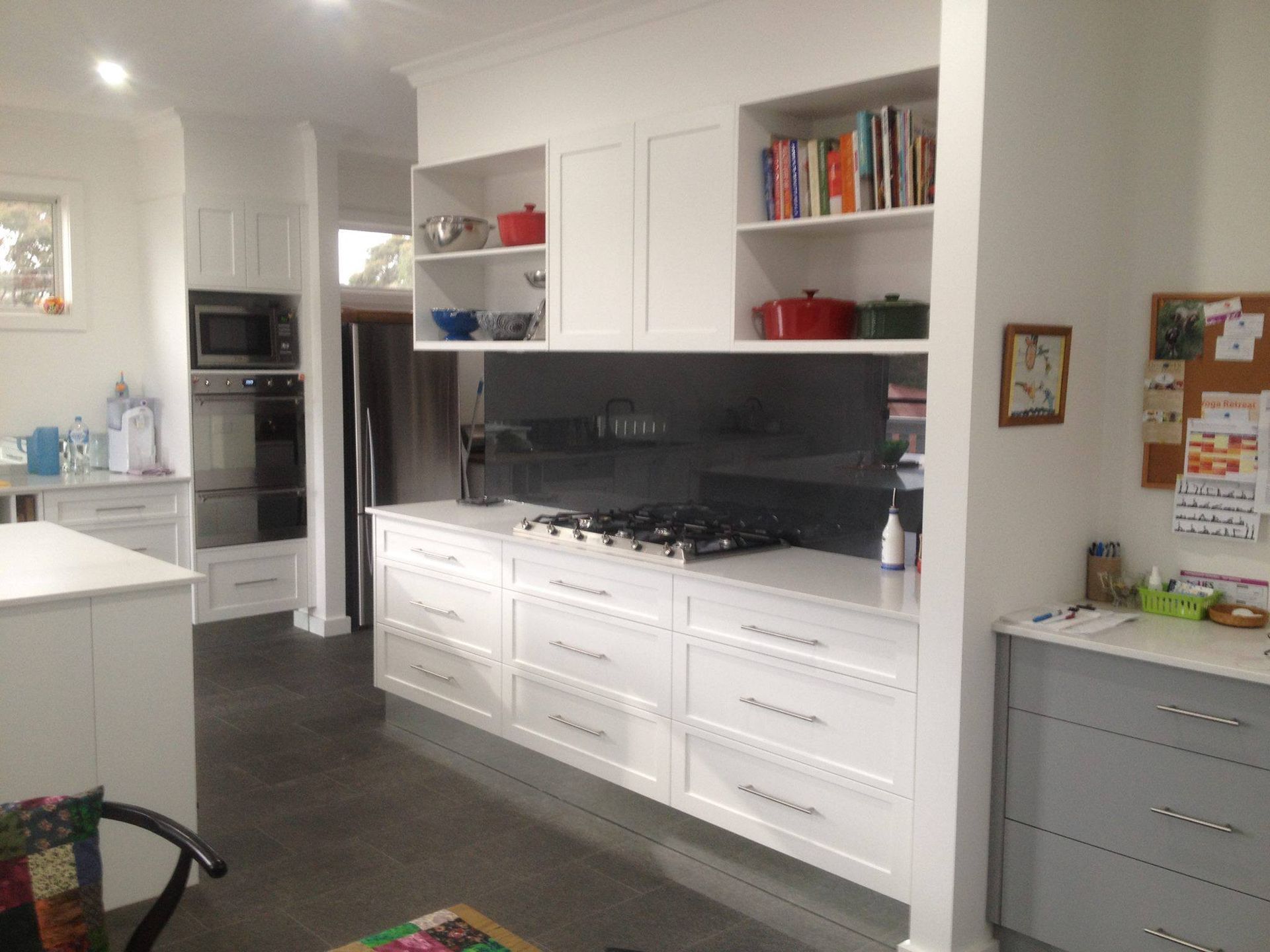 White kitchen with cabinets, stove, and a stainless steel backsplash; dark gray floor.