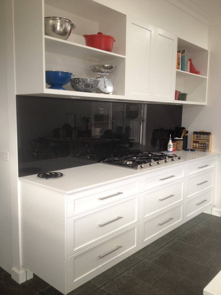 White kitchen with black backsplash, gas stove, and overhead cabinets with cooking items.