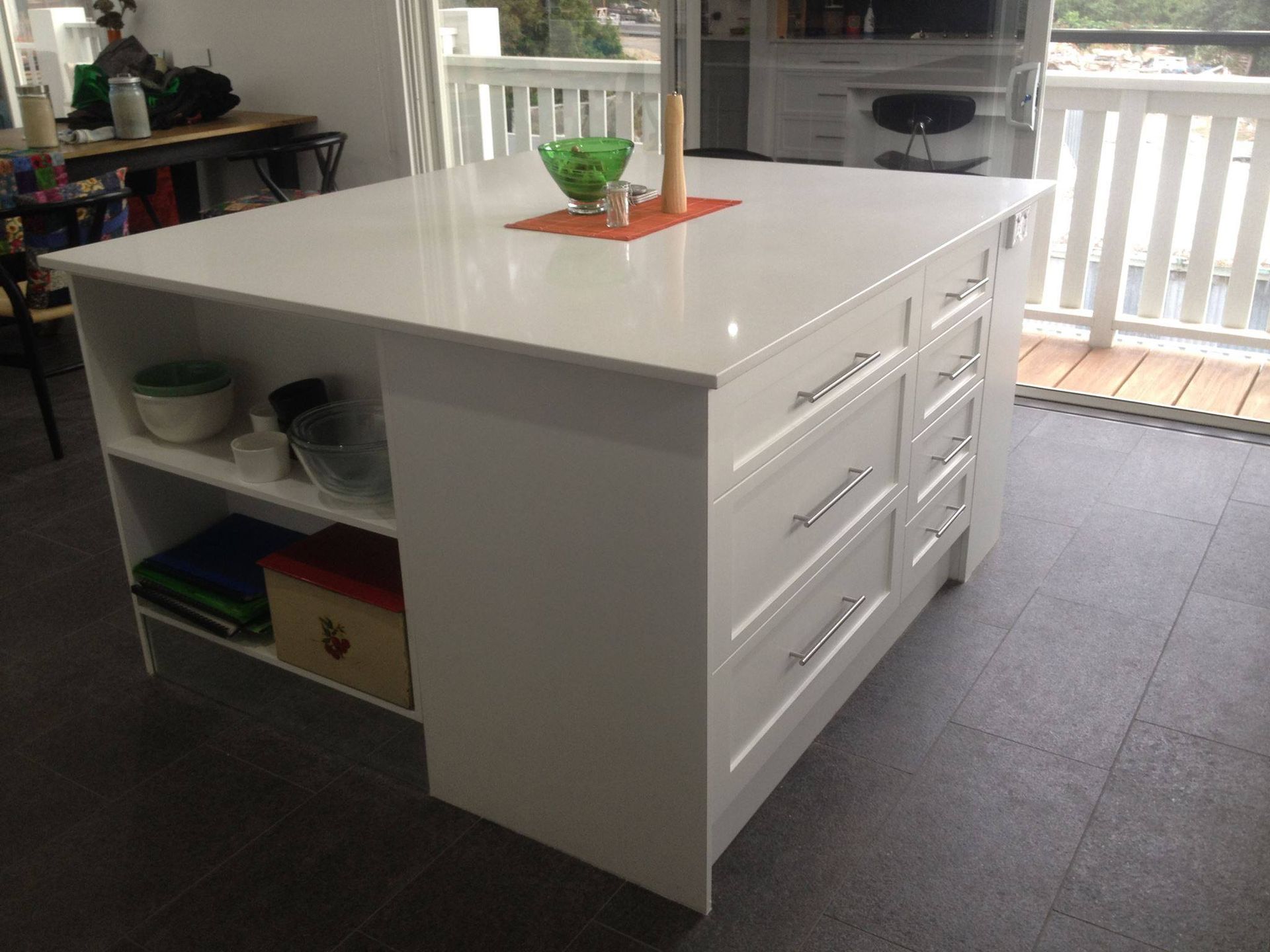 White kitchen island with drawers, shelves, and countertop; glass bowl and decor on top.