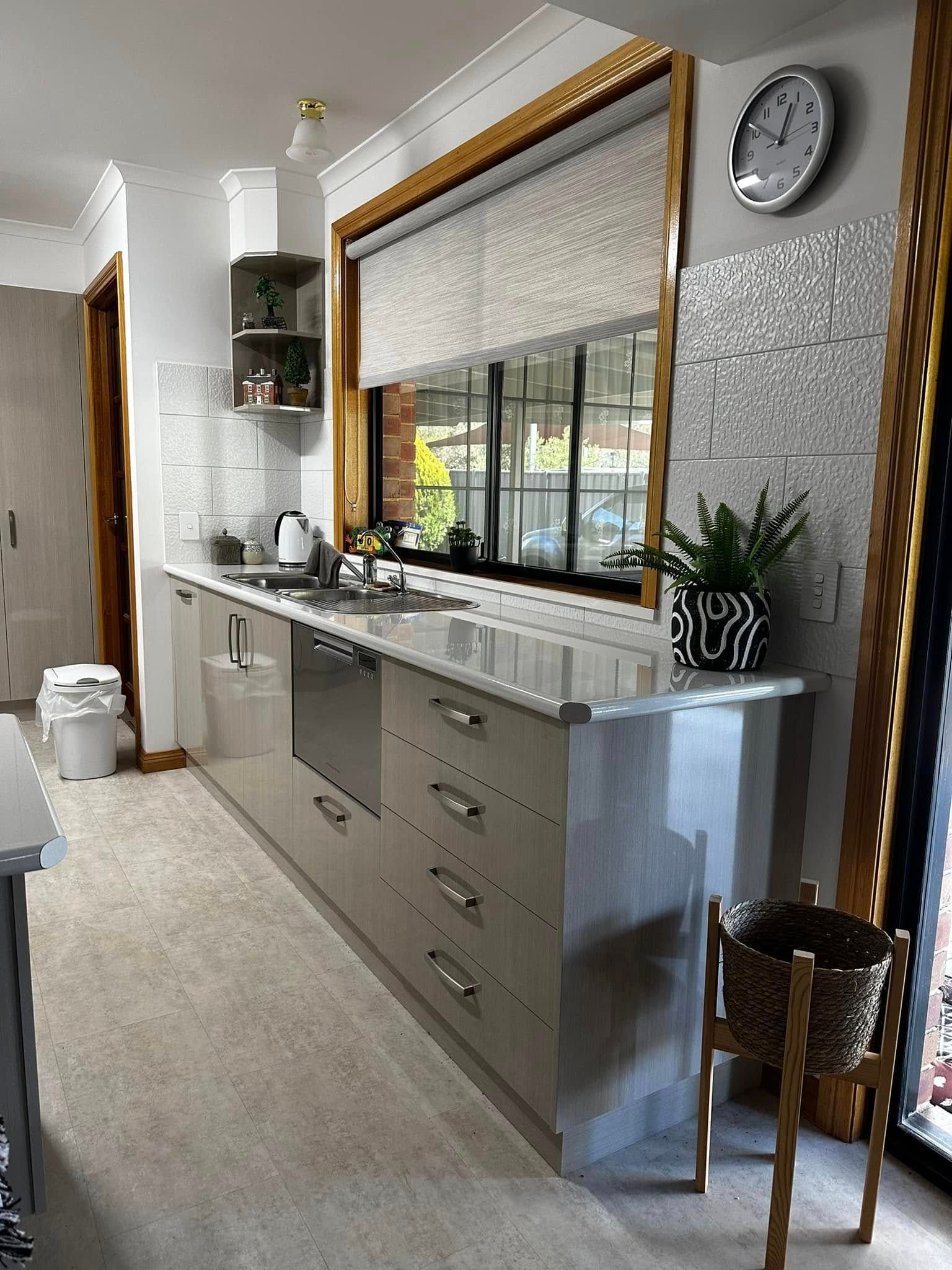 Modern kitchen with light gray cabinets, sink, and large window with roller blind.