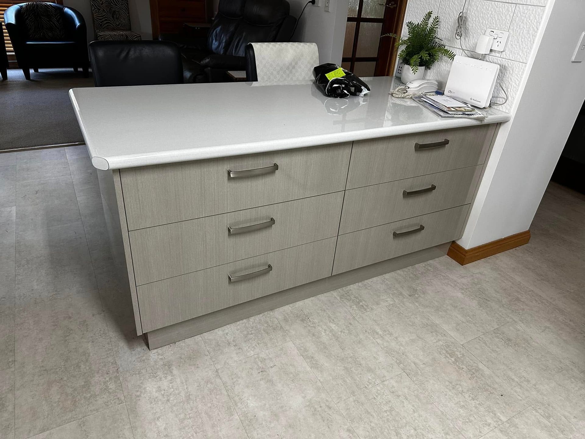 A kitchen island with gray drawers and a white countertop. There is a phone and plants on the counter.