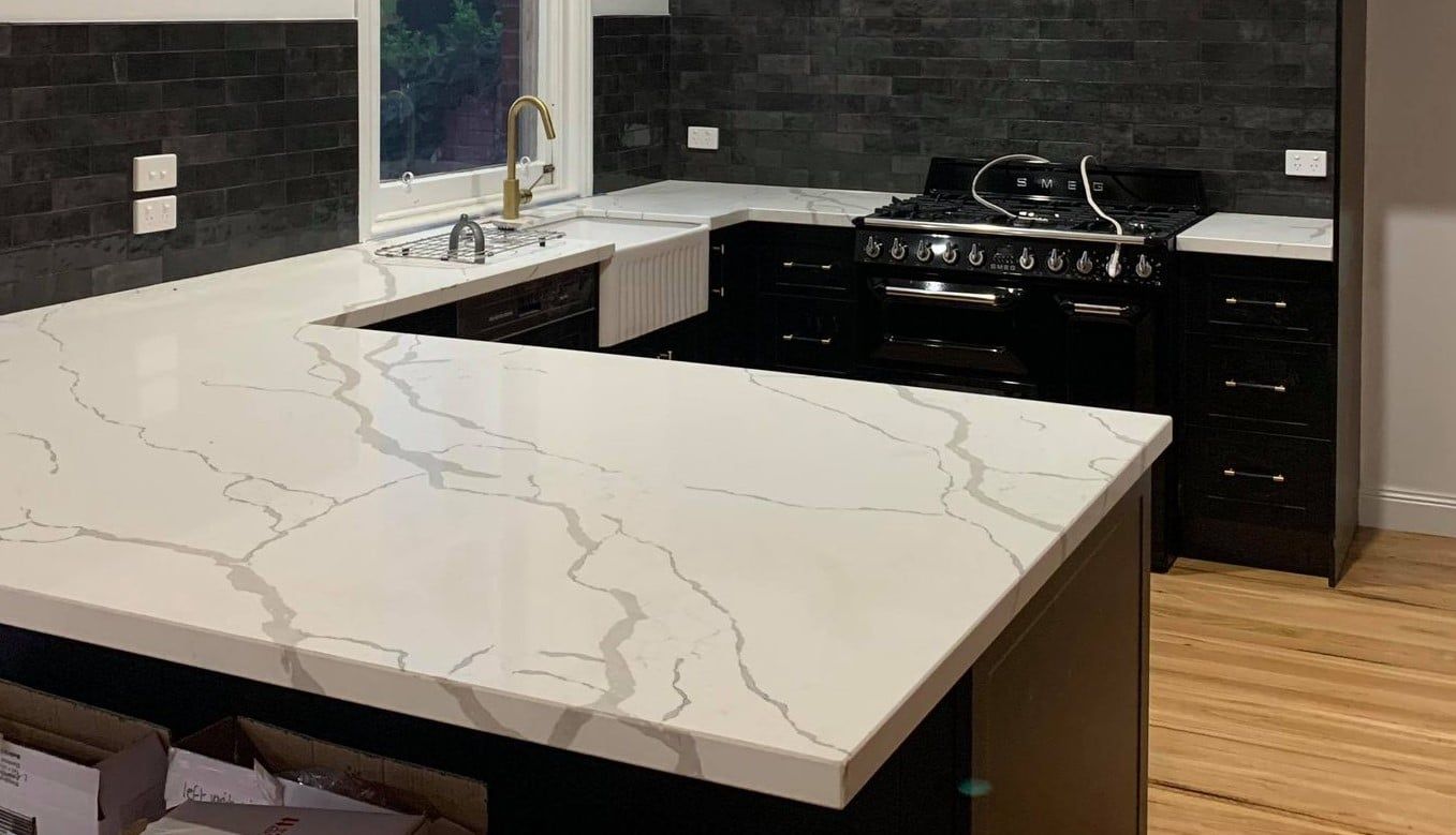 Kitchen with black cabinets, white countertop, and black tiled backsplash.