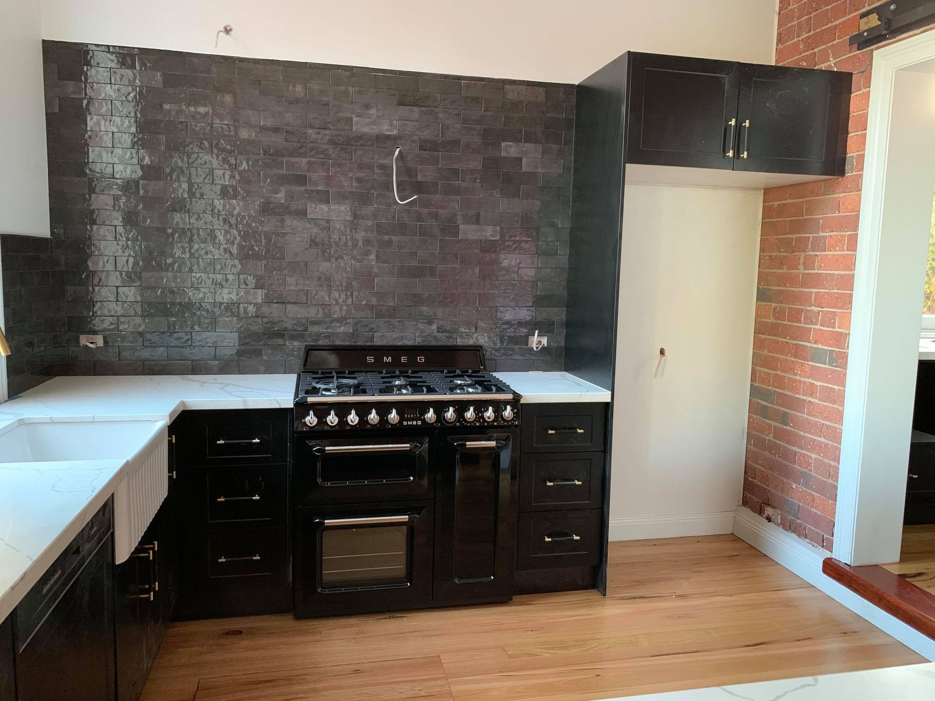Black kitchen with tile backsplash, dark cabinets, range, and white countertops.