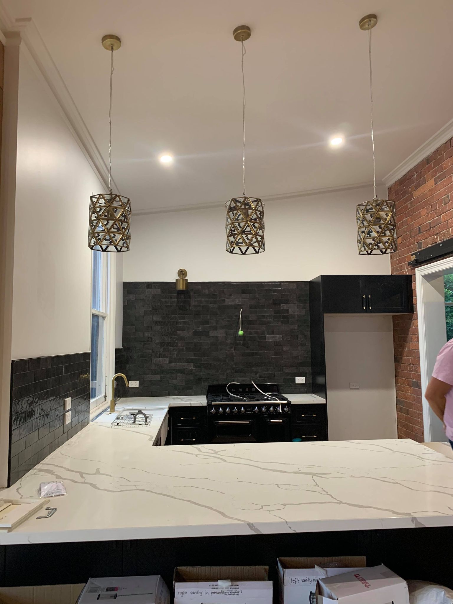 Kitchen renovation featuring dark cabinets, black tile backsplash, and three decorative pendant lights over the stovetop.