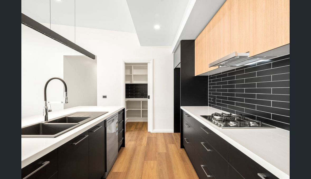Modern kitchen with black and wood cabinets, white countertops, and wooden flooring.