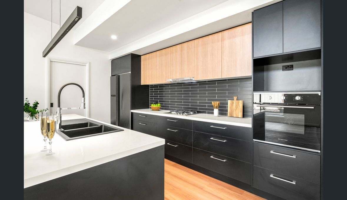 Modern kitchen with black cabinetry, light wood uppers, white countertops, and stainless steel appliances.