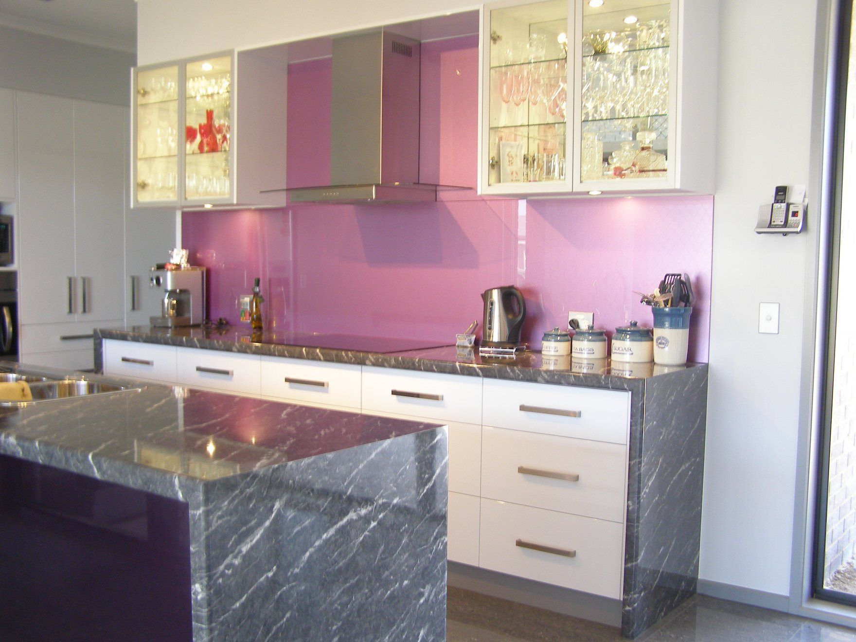 Modern kitchen with purple backsplash and marble countertops; white cabinets and island.