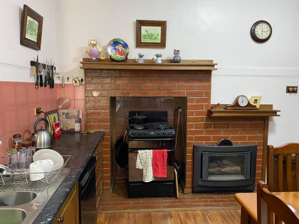 Kitchen with brick fireplace, stove, and sink; various items on shelves and walls.