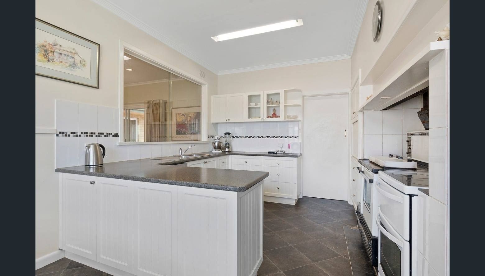 White kitchen with dark gray countertop and cabinets, built-in oven, and a view into another room.