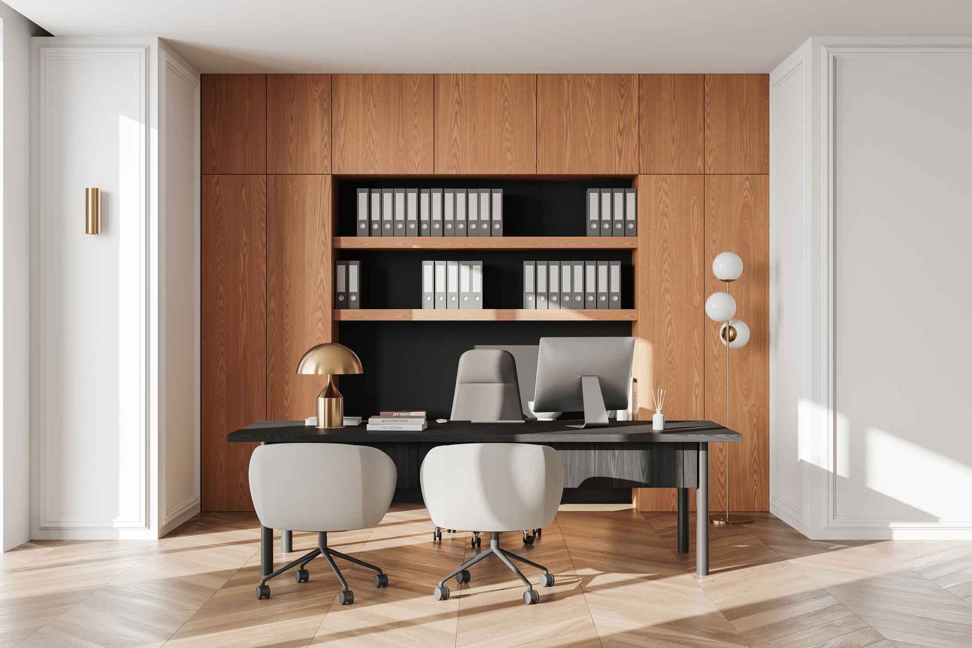 An office with a dark desk and wood paneling. Two white chairs sit in front of a computer and desk lamp.