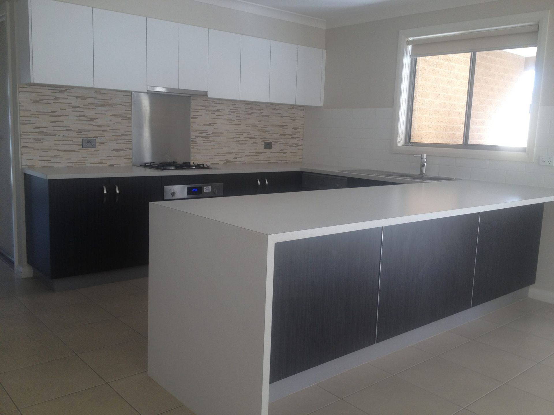 Modern kitchen with white and dark cabinets, a white countertop island, and a beige tiled backsplash.