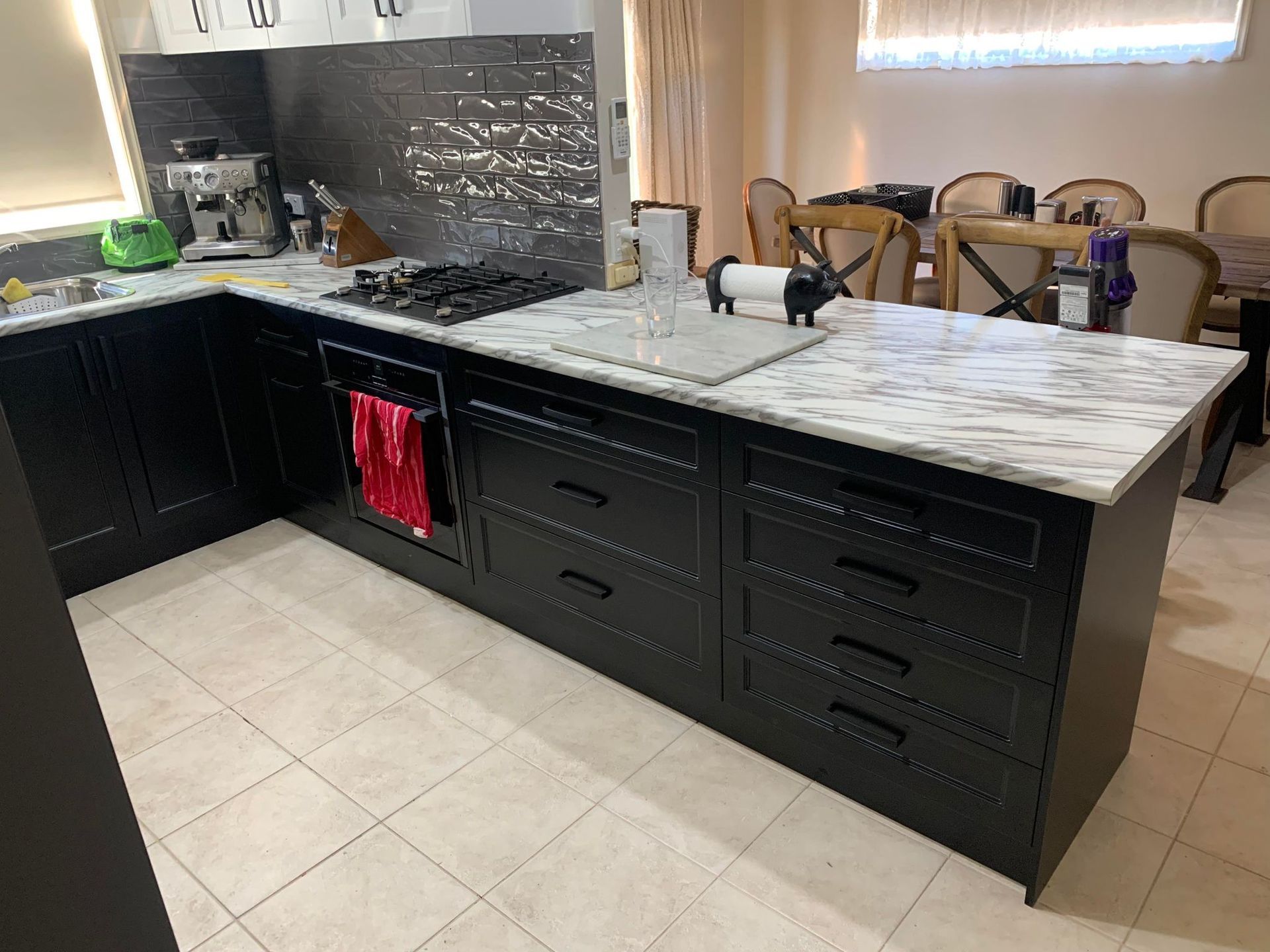 Black kitchen island with marble countertop, drawers, and stovetop.  A red towel hangs from a drawer.