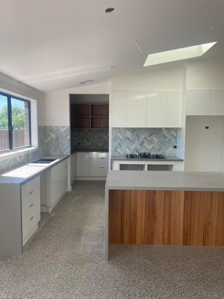 Modern kitchen with white cabinetry, wood island, and gray countertops, with patterned tile backsplash and terrazzo floors.