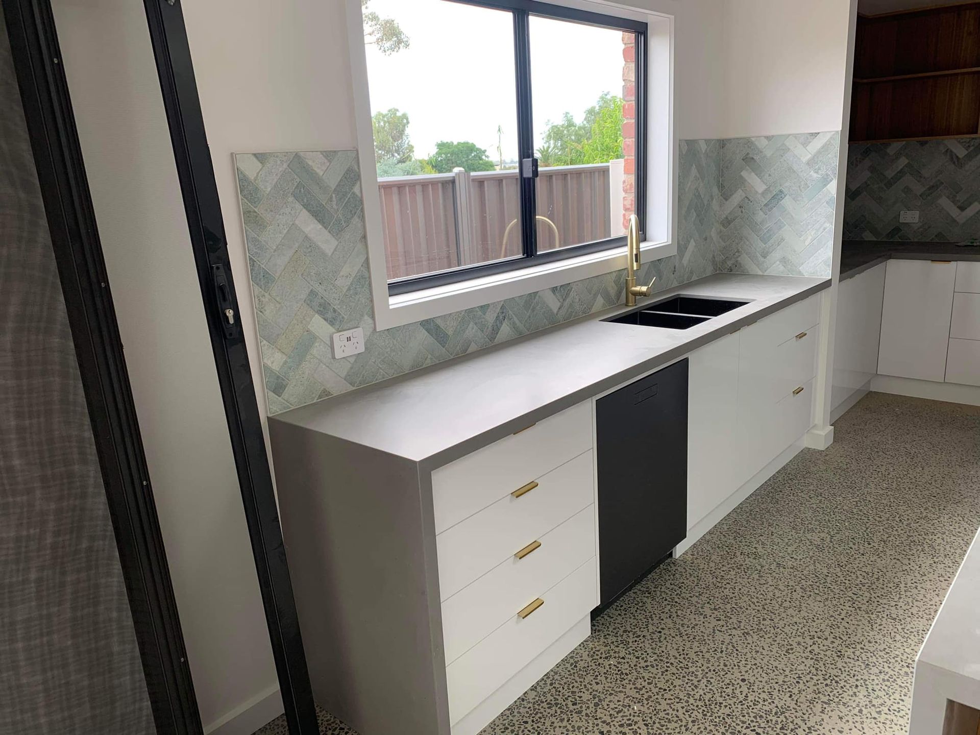 Modern kitchen with white cabinets, gray countertop, and patterned backsplash. Gold fixtures.