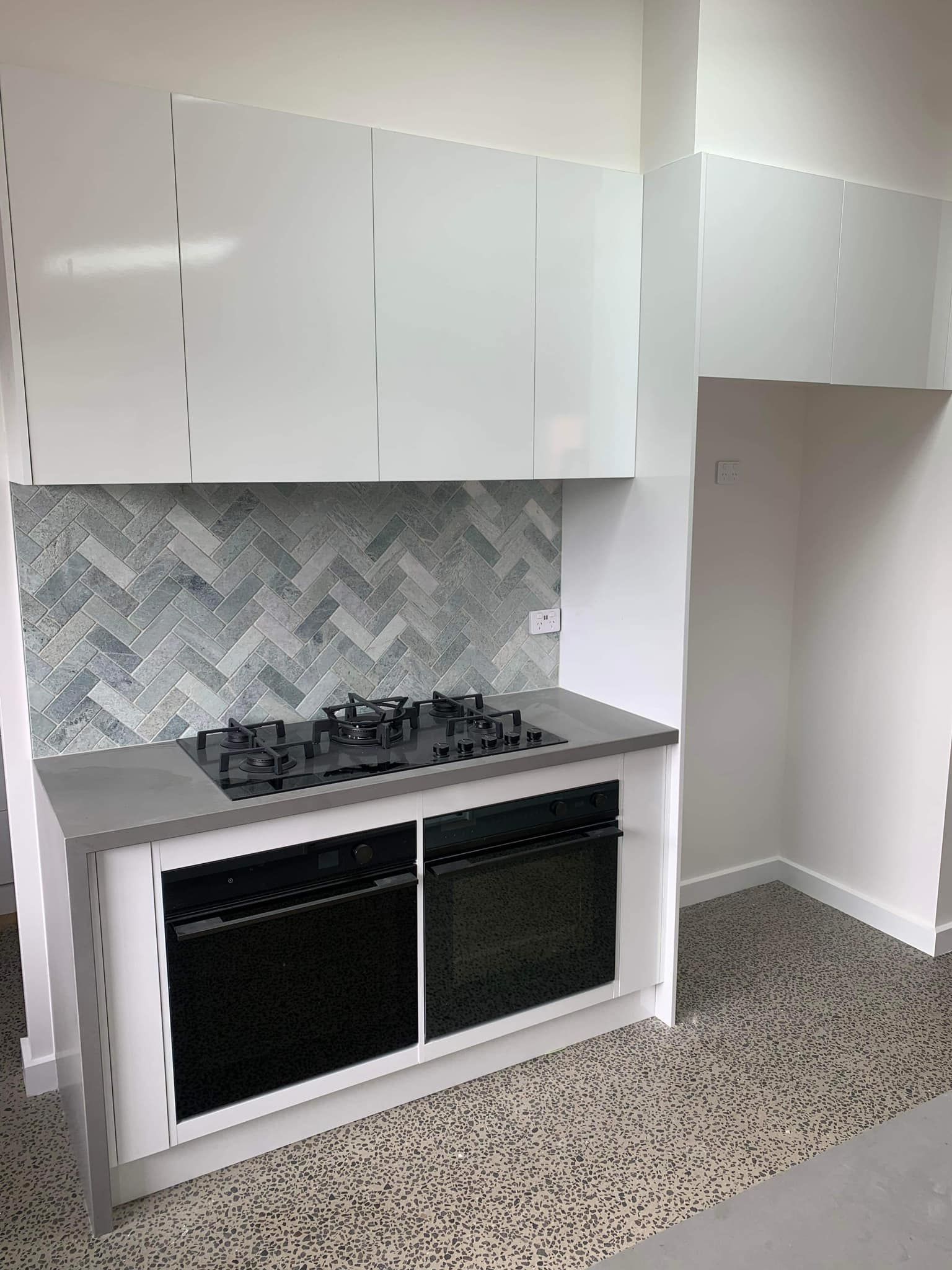 Modern kitchen with white cabinets, built-in oven, gas cooktop, gray countertop, and patterned backsplash.