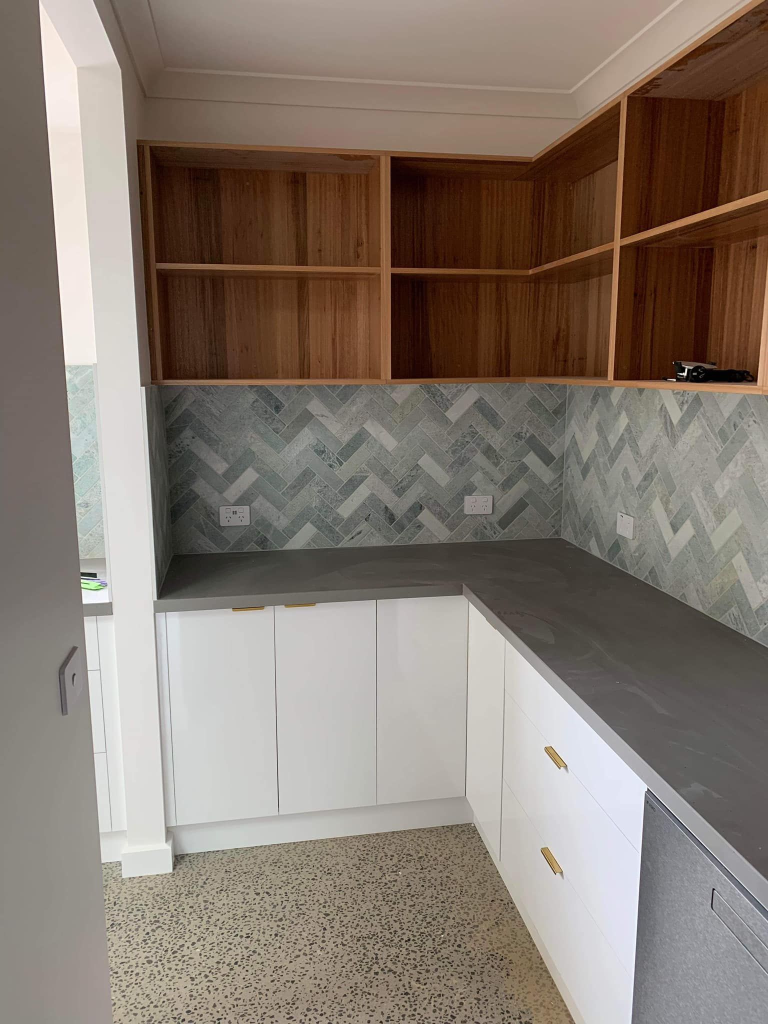 Kitchen corner with white cabinets, gray countertop, and wood shelves. Gray and blue backsplash.