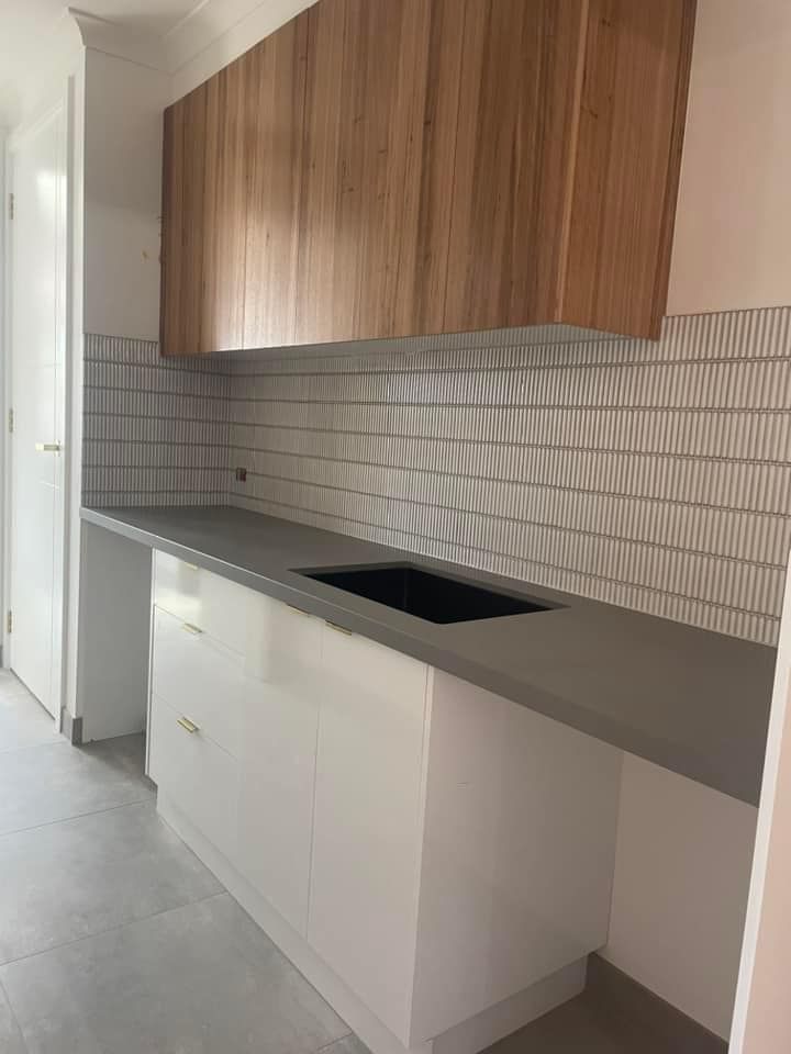 Modern kitchen with white cabinets, gray countertop, wood upper cabinet, and patterned backsplash.