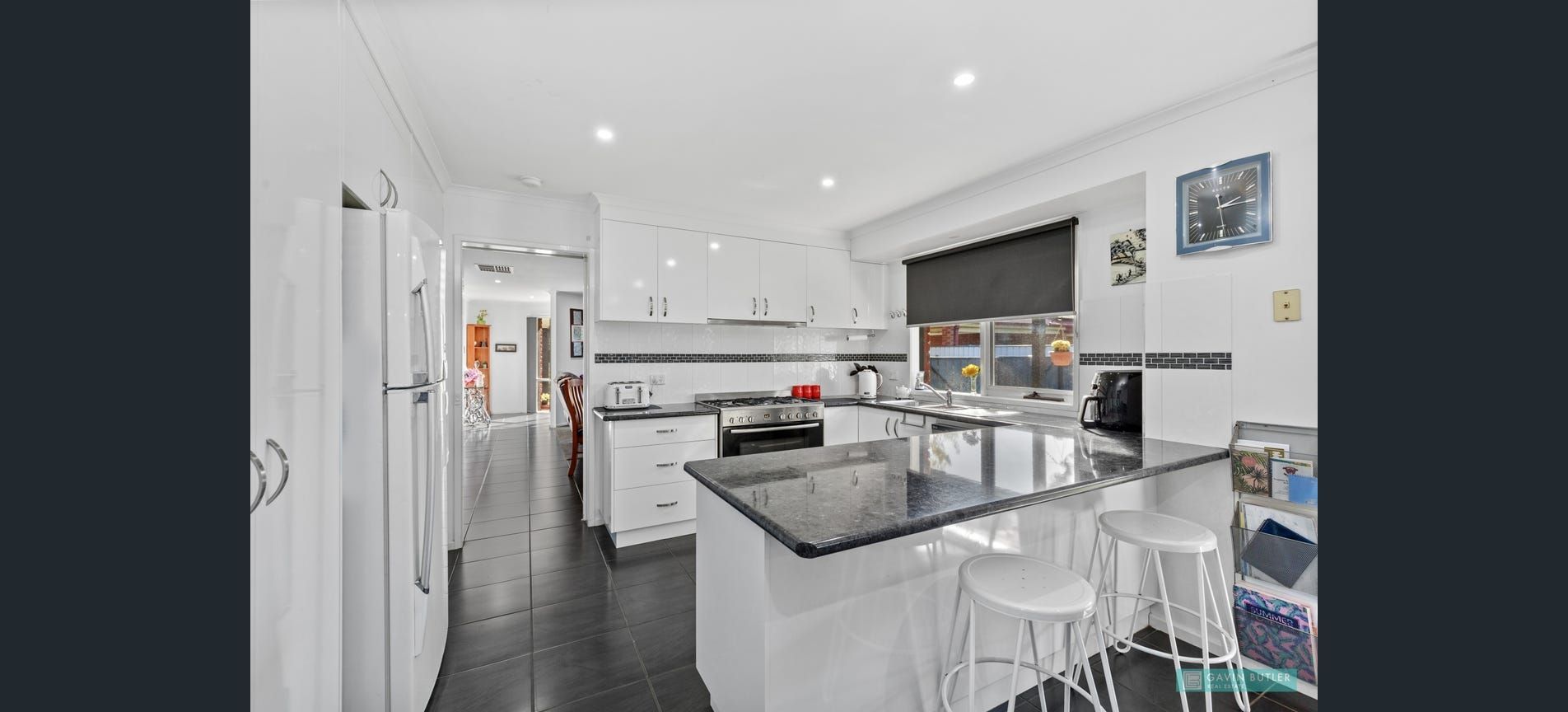 White kitchen with black countertops, island with stools, and view to another room.