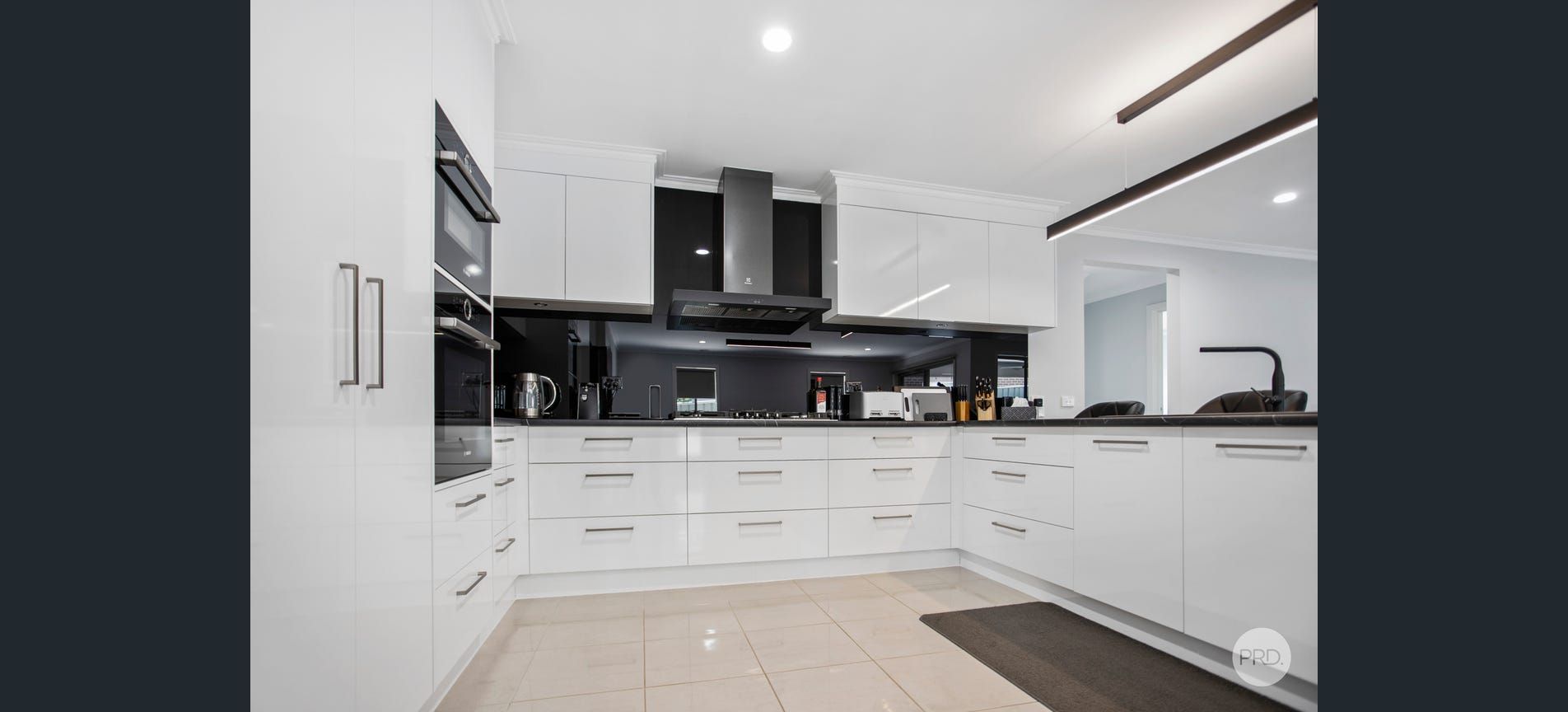 Modern white kitchen with glossy cabinets, stainless steel appliances, and dark countertops.