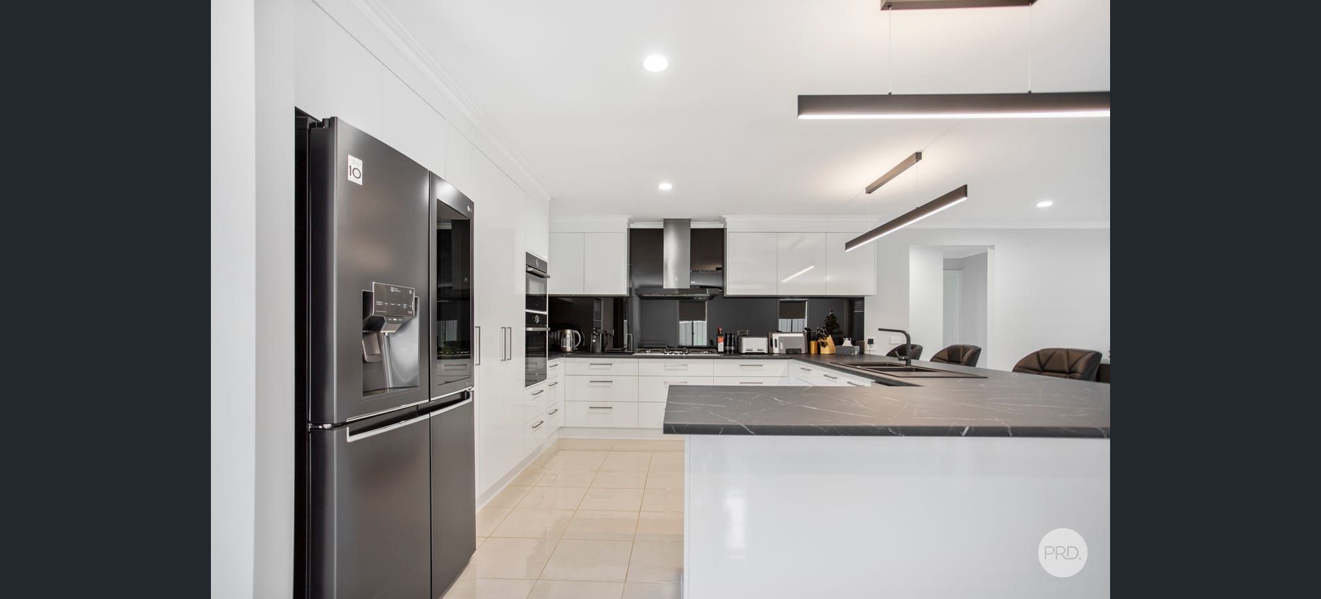 Modern kitchen with white cabinets, dark island countertop, and stainless steel refrigerator.