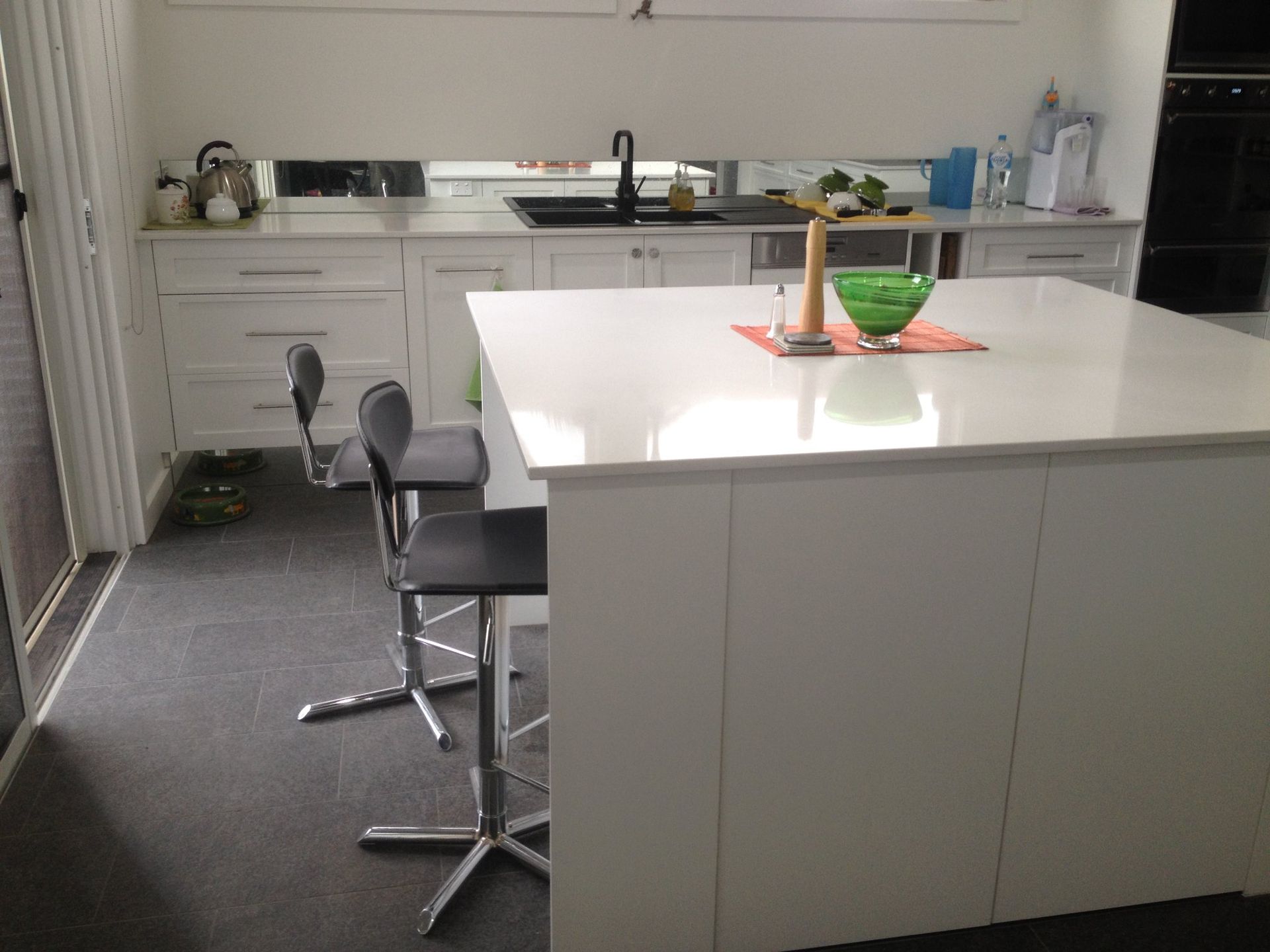 Modern white kitchen with island, black stools, and sink.
